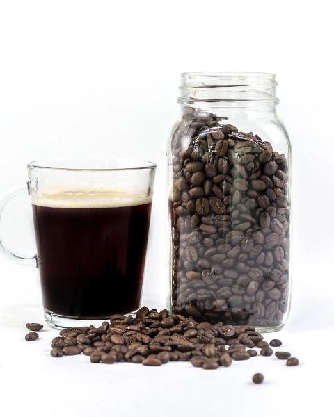 Glass of black coffee beside a jar of whole beans